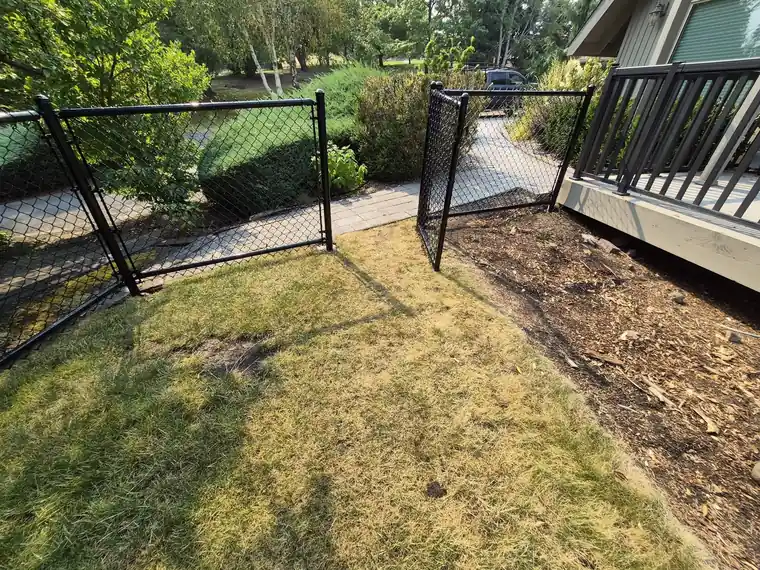 Black chain link fence and walk gate beside a deck and lawn