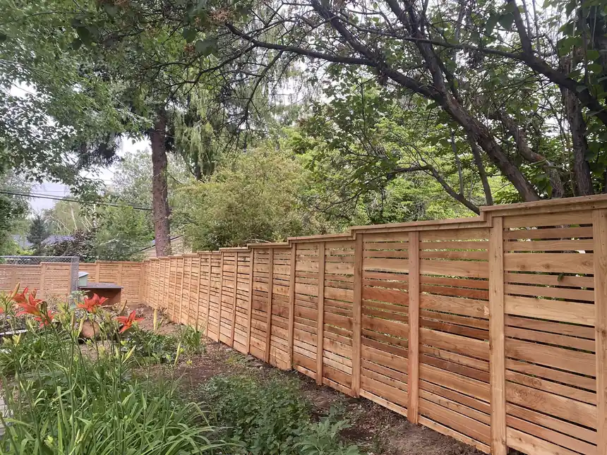 Long horizontal-board cedar privacy fence stepping down a garden line