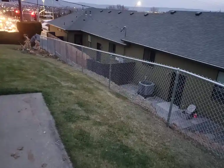 Chain link fence running down a slope above rooftops at dusk