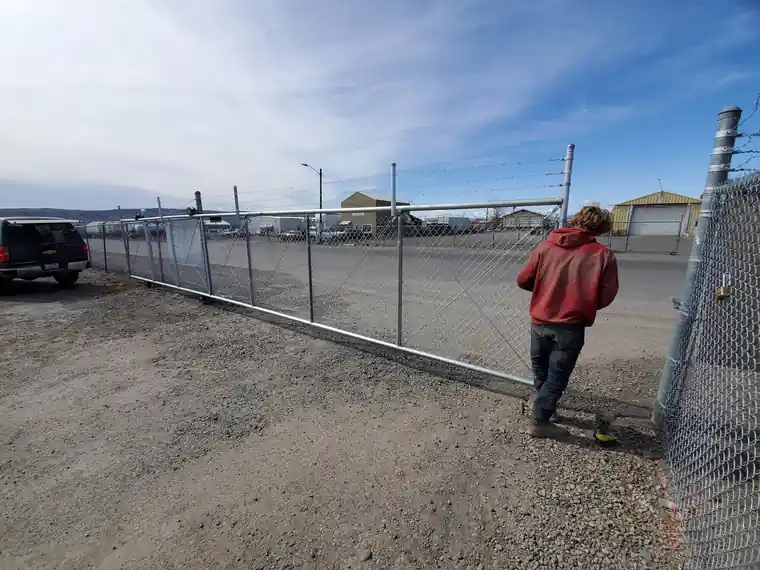A crew member, back to the camera, beside a long galvanized commercial chain link run with a gate